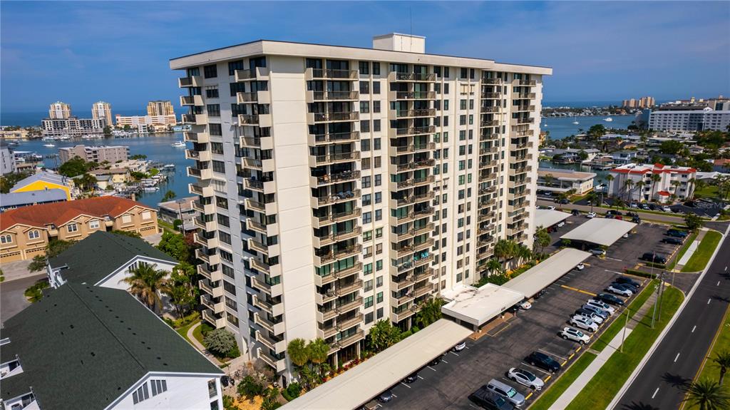 An aerial view shows a tall residential apartment building with balconies next to a parking lot — 400 ISLAND WAY UNIT 212, CLEARWATER BEACH, FL