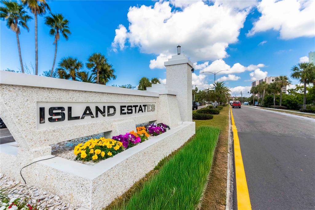A stone monument sign for Island Estates sits beside a road with palm trees — 400 ISLAND WAY UNIT 212, CLEARWATER BEACH, FL