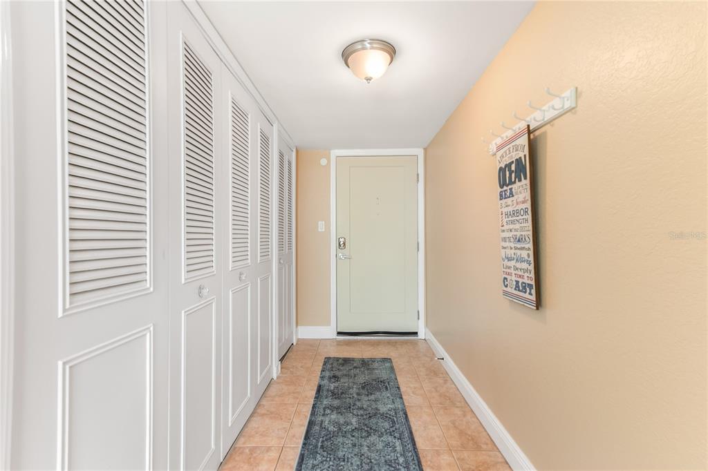 An entryway features white louvered closet doors, a beige door, and a wall-mounted sign — 400 ISLAND WAY UNIT 212, CLEARWATER BEACH, FL