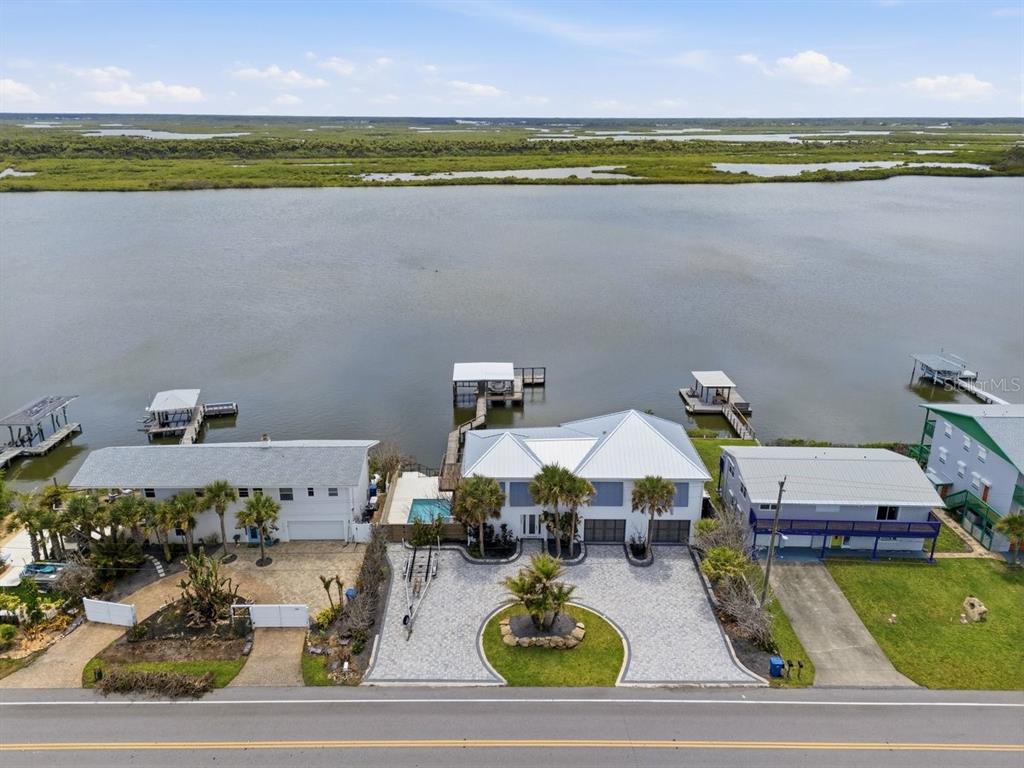 An aerial view shows three waterfront houses with private docks along a large body of water — 7050 TURTLEMOUND ROAD, NEW SMYRNA BEACH, FL