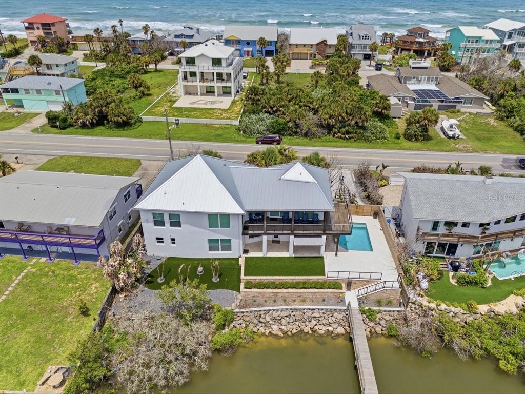 An aerial view shows a waterfront house with a pool, deck, and metal roof — 7050 TURTLEMOUND ROAD, NEW SMYRNA BEACH, FL
