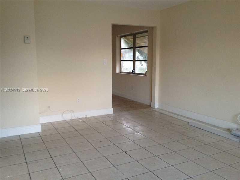 An empty room with light-colored walls and tiled flooring leads to a windowed area — HOLLYWOOD, FL