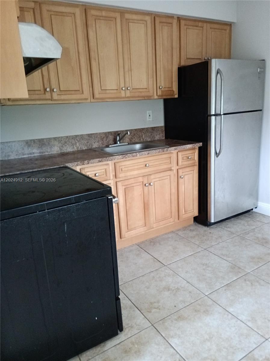 A kitchen features light wood cabinets, a stainless steel refrigerator, and a black stove — HOLLYWOOD, FL