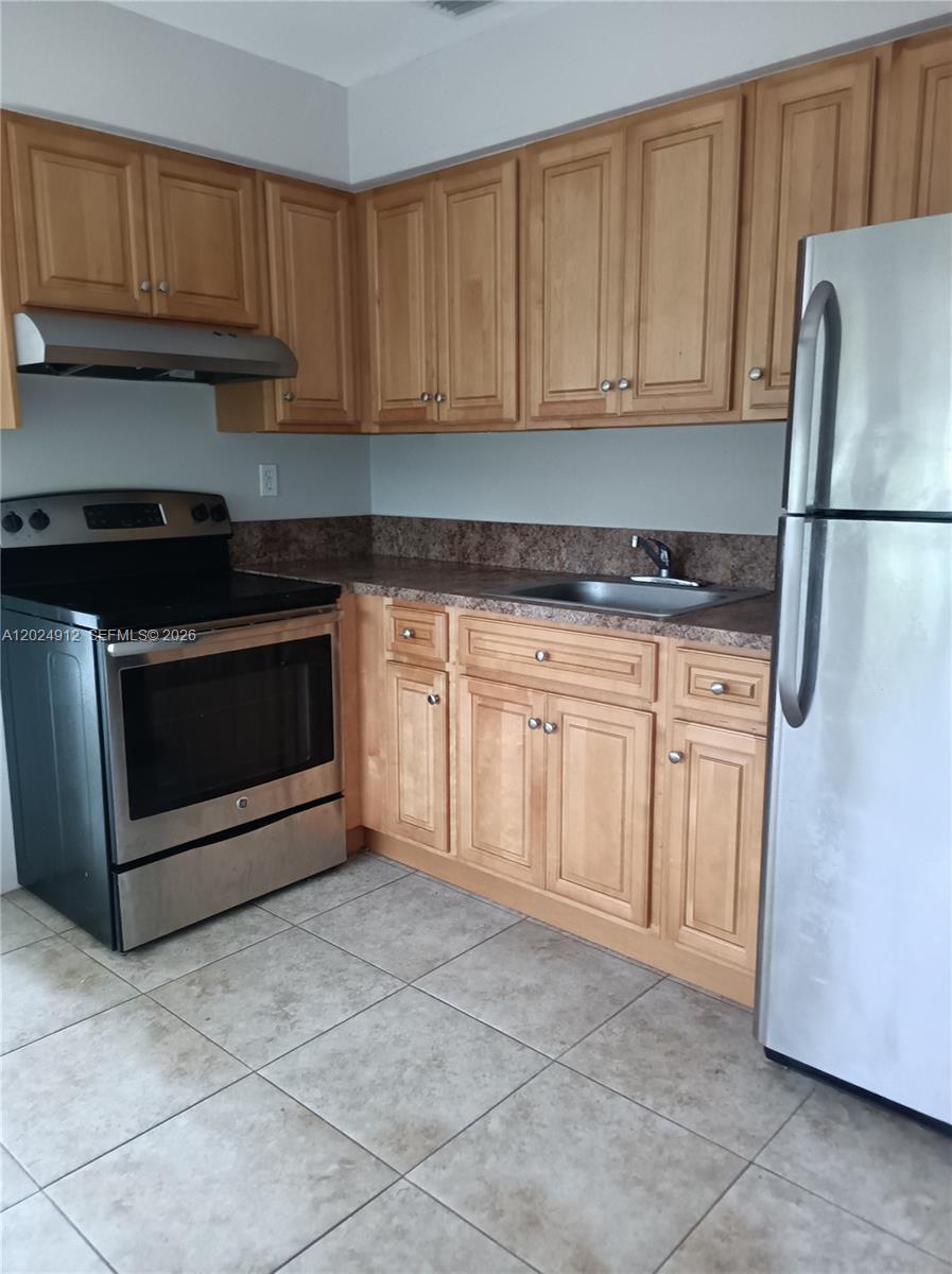 A kitchen features light wood cabinets, stainless steel appliances, and a brown laminate countertop — HOLLYWOOD, FL