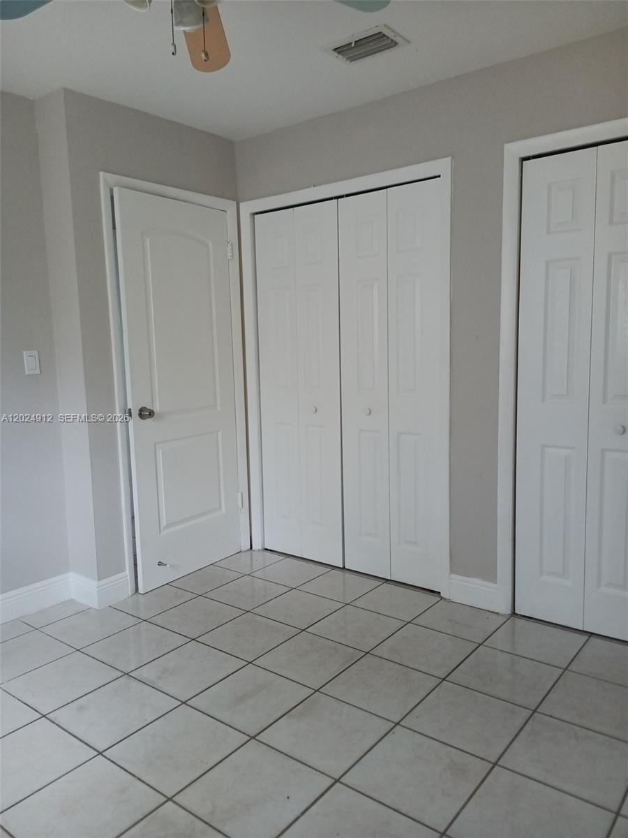 A room with light gray walls, white tiled flooring, and three white doors — HOLLYWOOD, FL