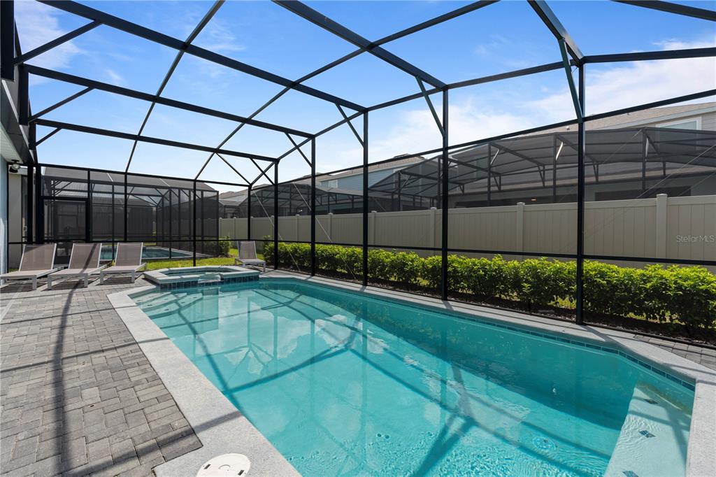 A screened-in swimming pool and hot tub sit on a paved patio with lounge chairs — 3625 LILY LANE, DAVENPORT, FL