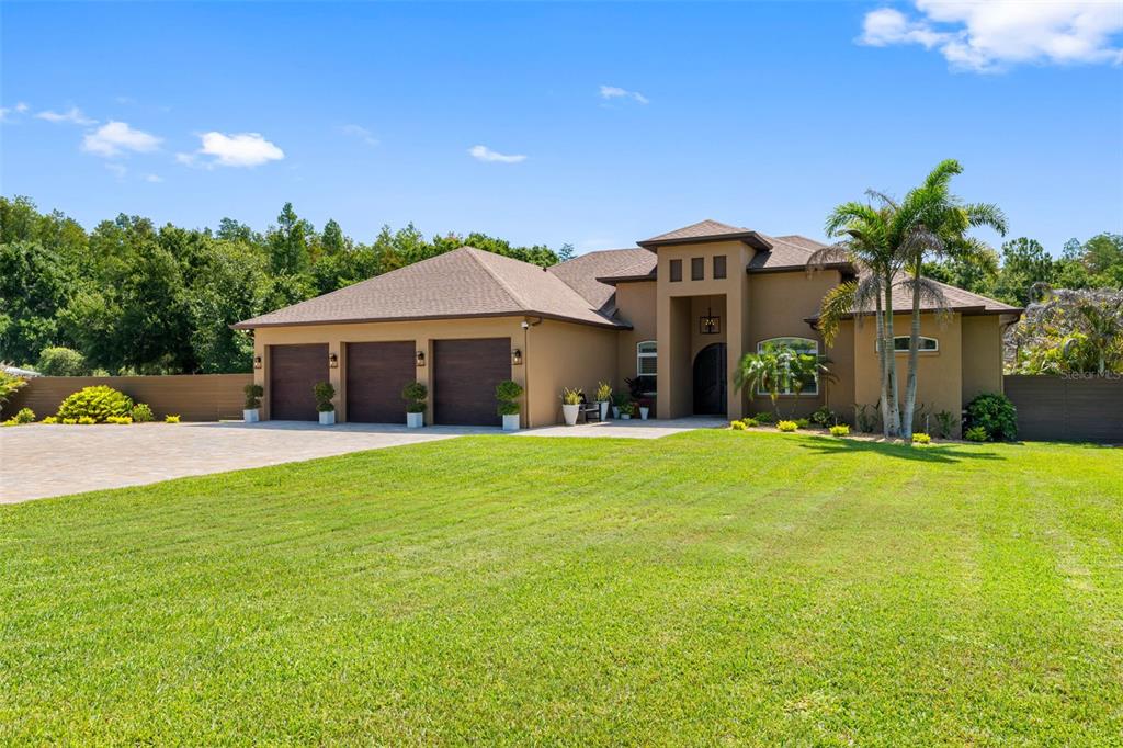 A tan single-story house with a three-car garage and a large front lawn — 17117 LAKESHORE ROAD, LUTZ, FL