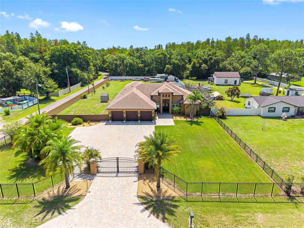 An aerial view shows a single-story house with a three-car garage and gated driveway — 17117 LAKESHORE ROAD, LUTZ, FL