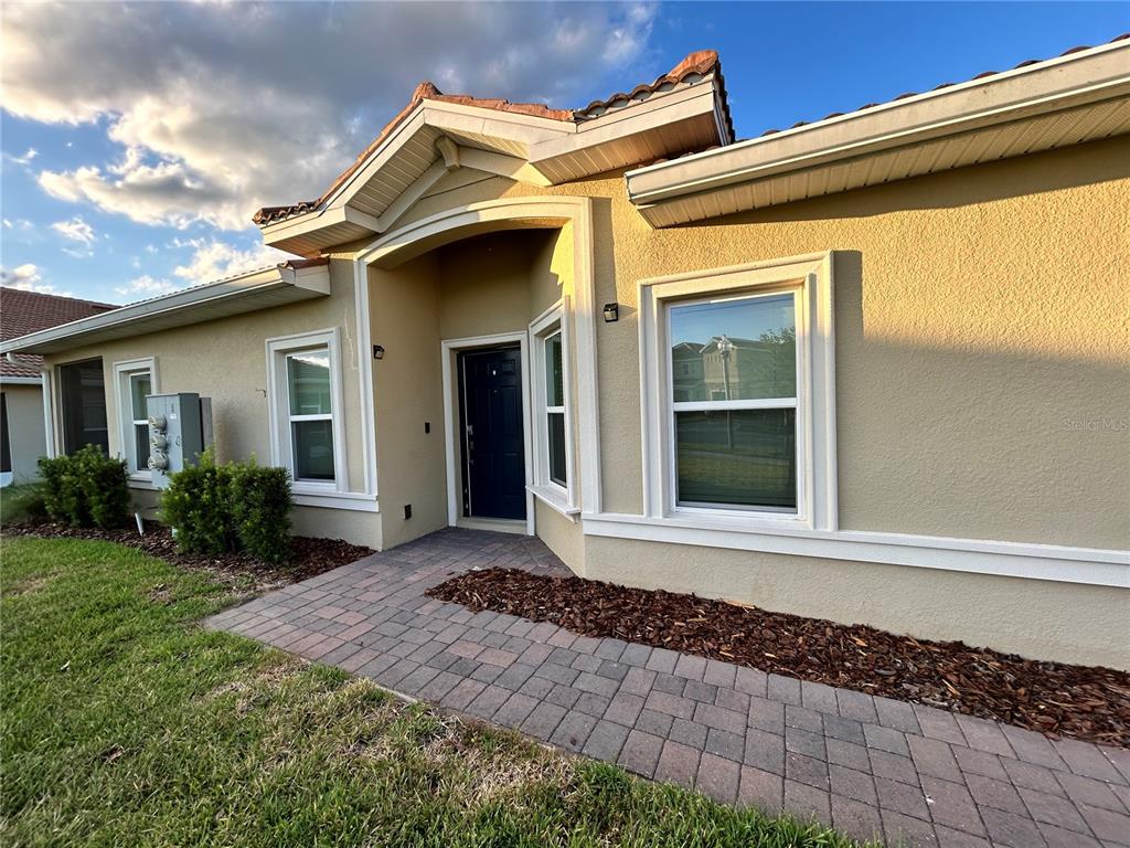A beige stucco house exterior features a dark front door, white trim, and paver walkway — 1159 TRAPPERS TRAIL LOOP, DAVENPORT, FL
