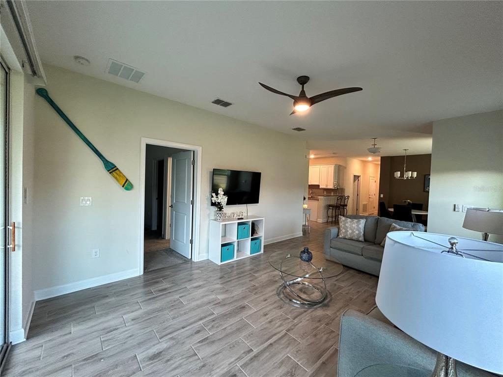 A living room features wood-look tile flooring, a ceiling fan, a television, and an oar decoration — 1159 TRAPPERS TRAIL LOOP, DAVENPORT, FL