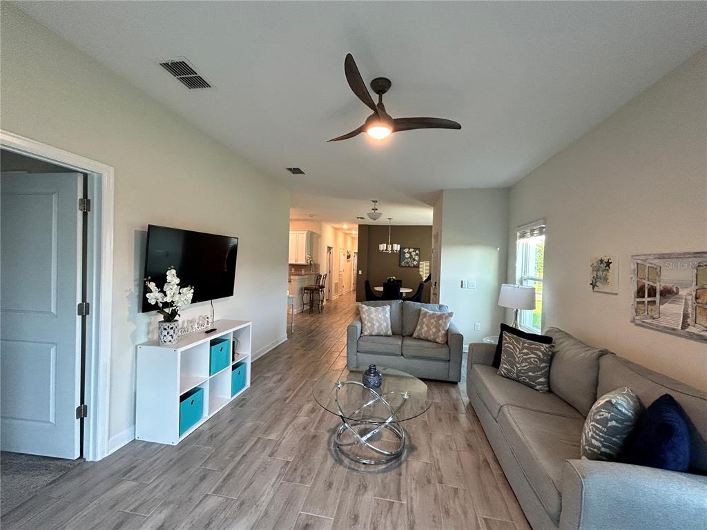 A living room with light wood-look tile floors, a ceiling fan, and a glass coffee table — 1159 TRAPPERS TRAIL LOOP, DAVENPORT, FL