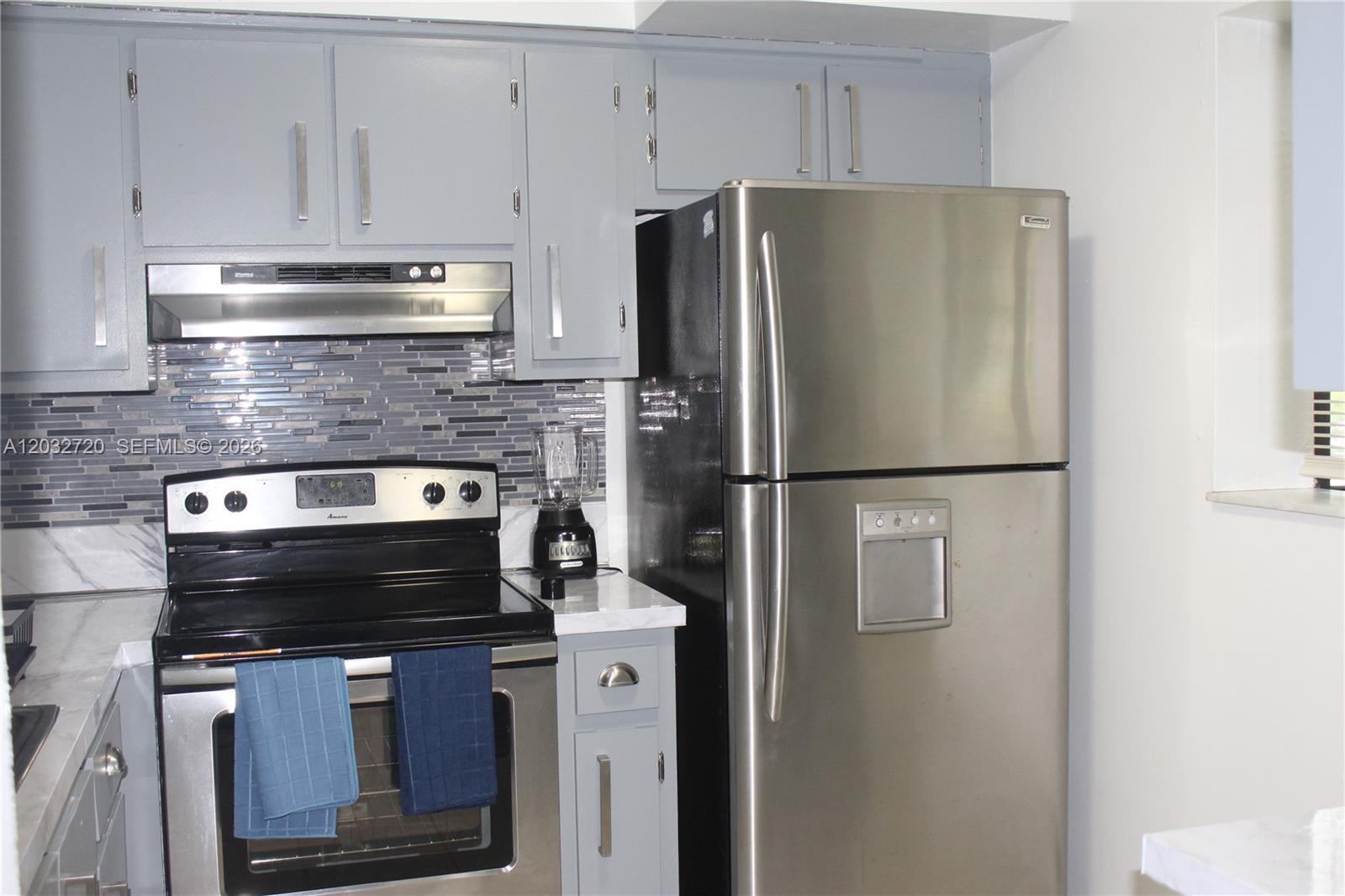A kitchen features gray cabinets, stainless steel appliances, and a tiled backsplash — 110 Gardens Dr # 103, Pompano Beach FL 33069, POMPANO BEACH, FL