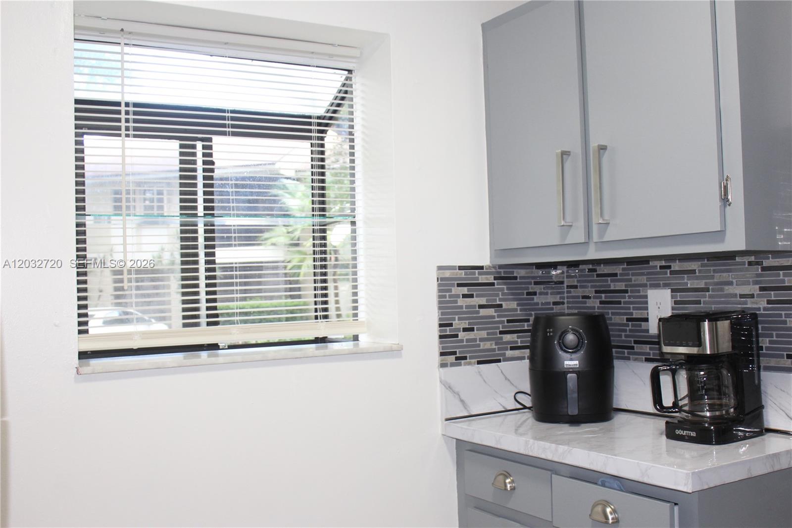A kitchen features gray cabinets, a marble-look countertop, a tiled backsplash, and a window — 110 Gardens Dr # 103, Pompano Beach FL 33069, POMPANO BEACH, FL