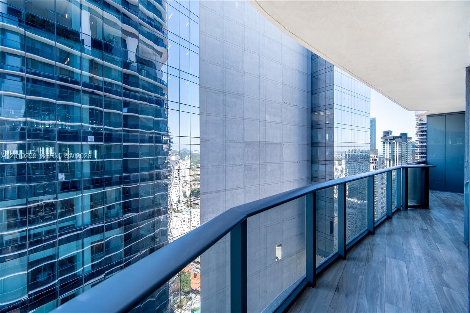 A balcony with wood-look tile flooring overlooks a narrow gap between two glass skyscrapers — 801 S Miami Ave # 3905, Miami FL 33130, MIAMI, FL