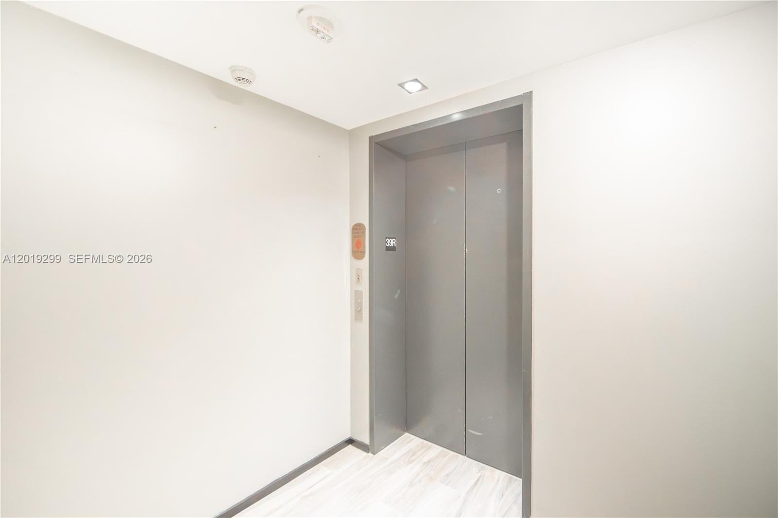 A gray elevator door is set into a plain white wall with light wood flooring — 801 S Miami Ave # 3905, Miami FL 33130, MIAMI, FL