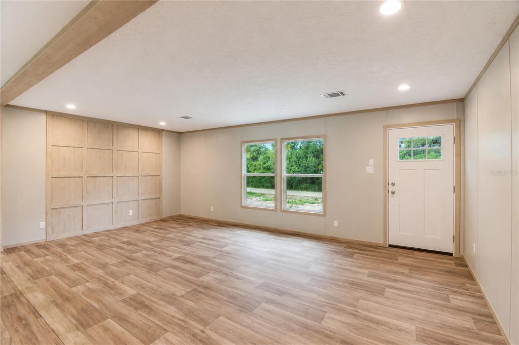 A living room features wood-look flooring, a paneled accent wall, and a white exterior door — 5235 SW 161ST CT ROAD, OCALA, FL