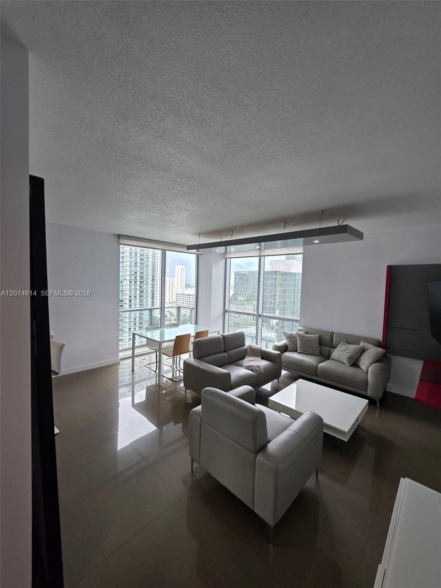A modern living and dining area features gray leather furniture, tile floors, and floor-to-ceiling windows — 1060 Brickell Ave # 2201, Miami FL 33131, MIAMI, FL