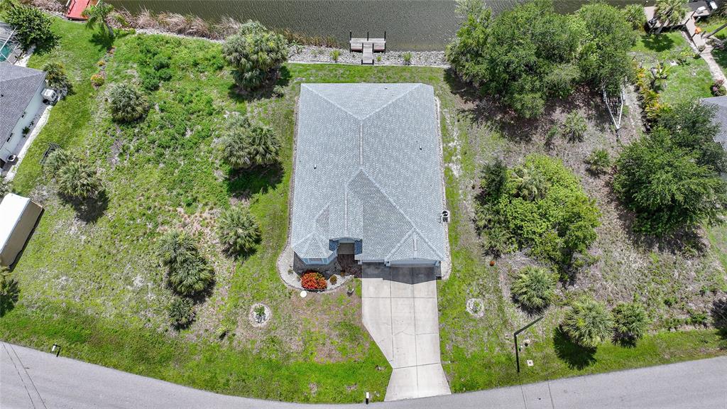 An aerial view shows a single-story house with a gray roof, driveway, and waterfront backyard — 9436 PRESIDENT CIRCLE, PORT CHARLOTTE, FL