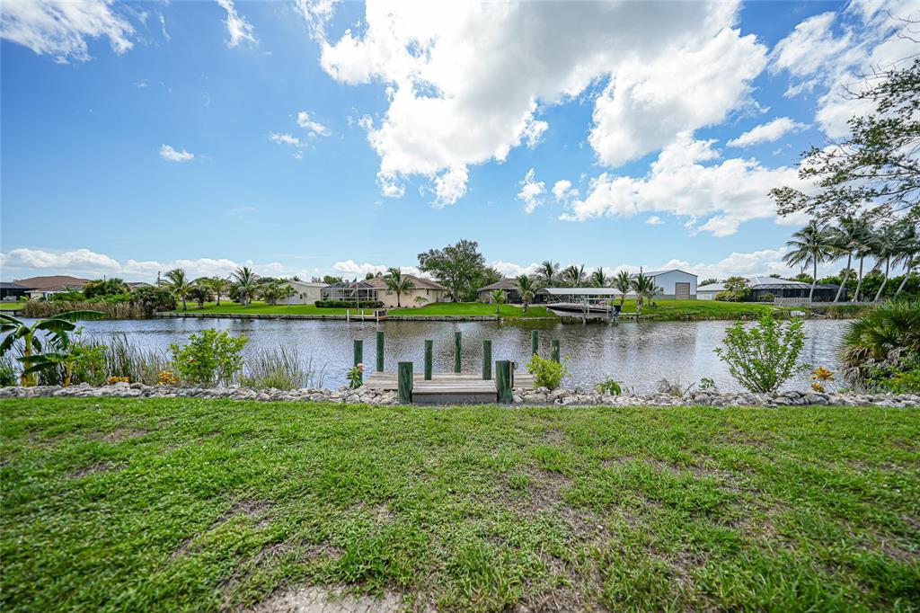 A grassy backyard overlooks a canal with a small wooden dock and a boat lift — 9436 PRESIDENT CIRCLE, PORT CHARLOTTE, FL