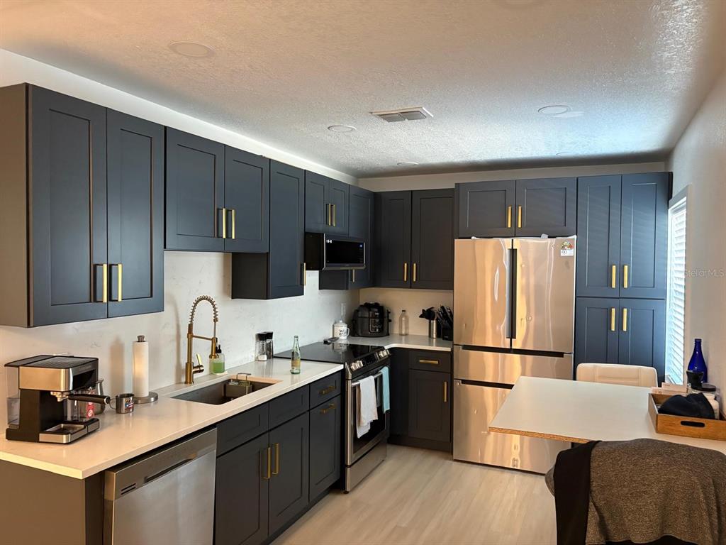 A kitchen features dark blue cabinets, stainless steel appliances, and white countertops — 215 ILLINOIS AVENUE, ST CLOUD, FL