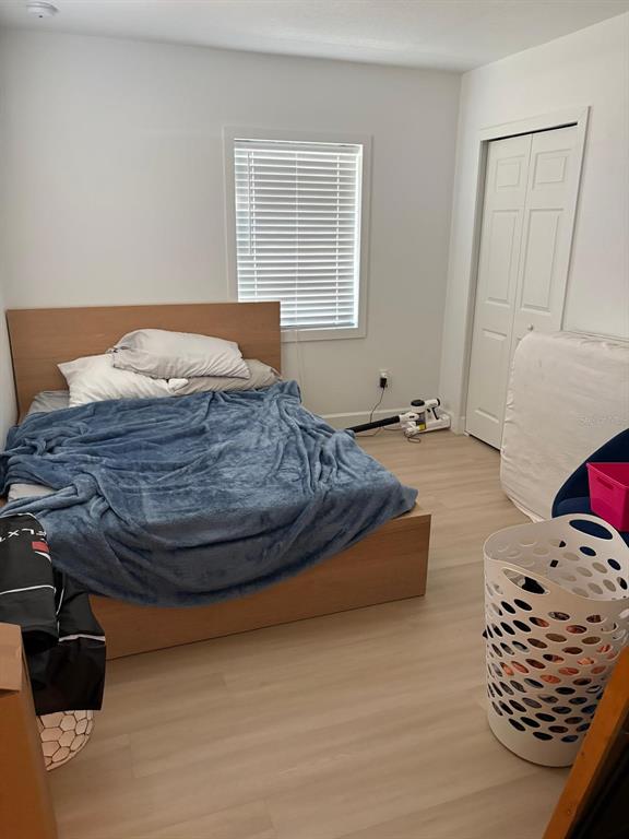 A bedroom features light wood-look flooring, a bed with a blue blanket, and a white closet — 215 ILLINOIS AVENUE, ST CLOUD, FL