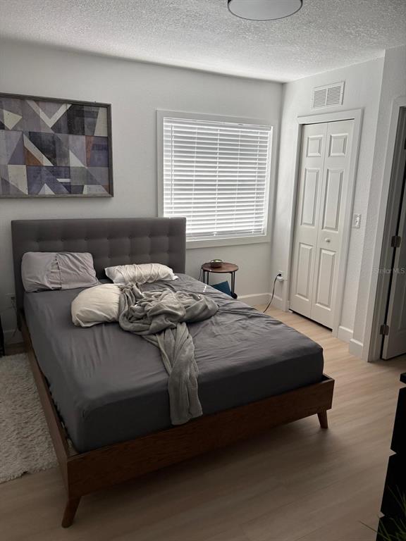 A bedroom with a grey tufted headboard, a wooden bed frame, and light wood flooring — 215 ILLINOIS AVENUE, ST CLOUD, FL