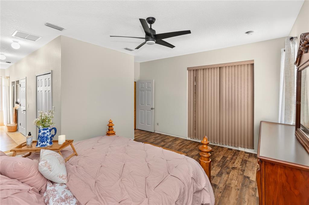 A bedroom features wood-look flooring, a ceiling fan, a pink bedspread, and vertical window blinds — 3393 BALTIC SEA BOULEVARD, TAVARES, FL