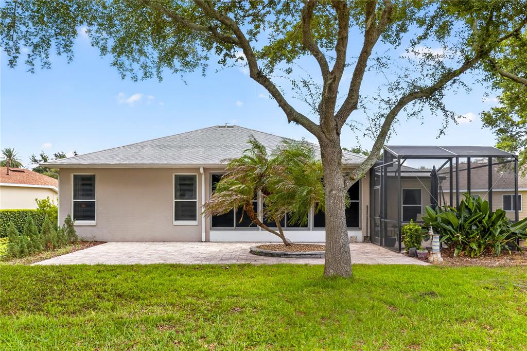 The rear exterior of a house features a paved patio, a screened enclosure, and landscaping — 3393 BALTIC SEA BOULEVARD, TAVARES, FL