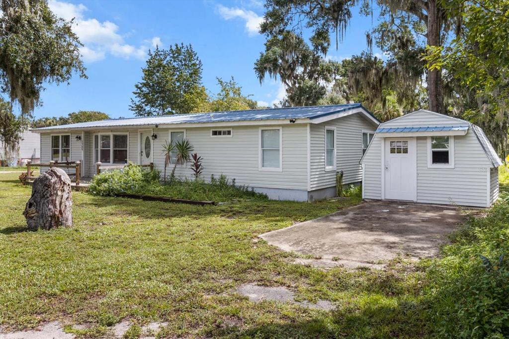 A light-colored single-story house with a metal roof and a detached shed on a lawn — 1955 CR 439C, LAKE PANASOFFKEE, FL