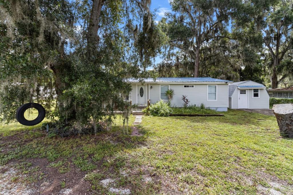 A single-story light gray house with a metal roof sits behind a large tree — 1955 CR 439C, LAKE PANASOFFKEE, FL