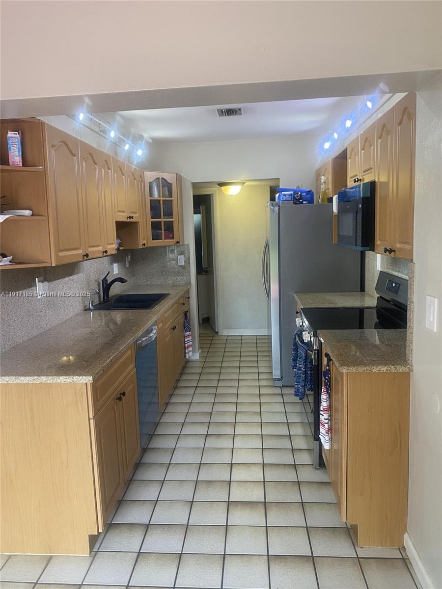 A galley kitchen features light wood cabinets, granite countertops, a black sink, and tiled floors — 4802 Bayberry Ln, Tamarac FL 33319, TAMARAC, FL