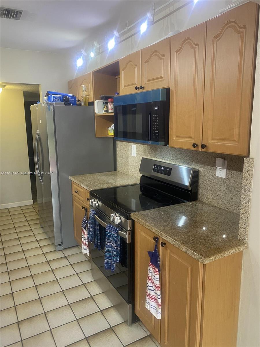 A kitchen features wood cabinets, granite countertops, stainless steel appliances, and light-colored tile flooring — 4802 Bayberry Ln, Tamarac FL 33319, TAMARAC, FL
