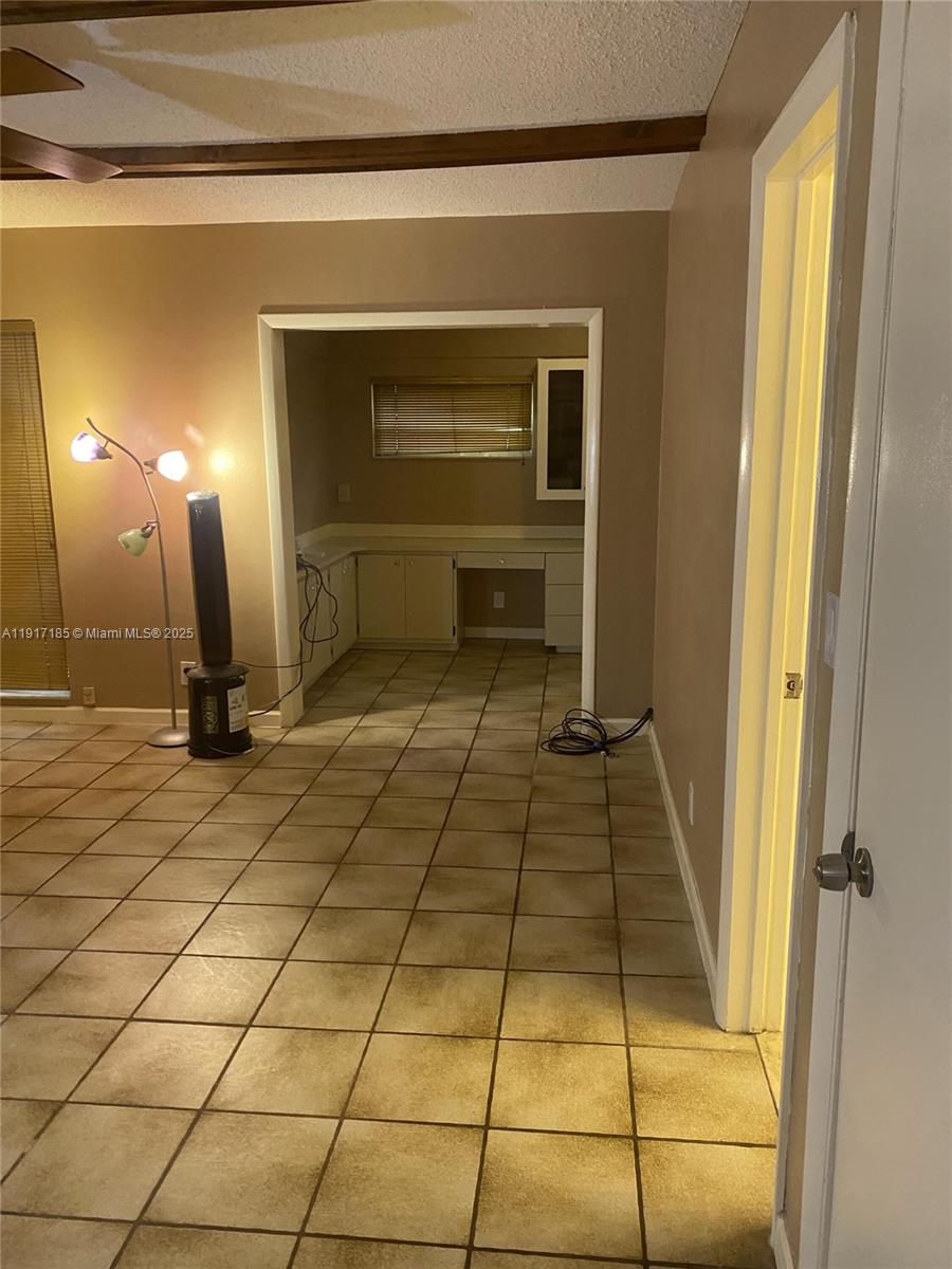 A room with tan tile flooring leads into a kitchen area with white cabinetry — 4802 Bayberry Ln, Tamarac FL 33319, TAMARAC, FL