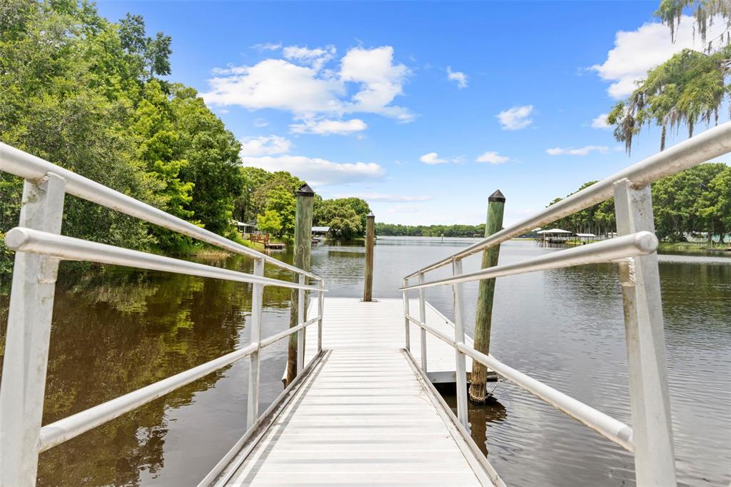 A metal dock extends over a calm lake surrounded by trees under a blue sky — 11420 E STEAMBOAT DRIVE, FLORAL CITY, FL