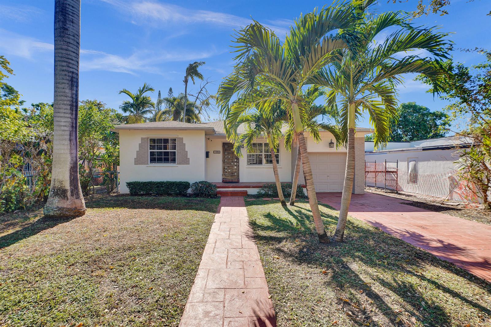 A single-story house with a paved walkway, palm trees, and a garage under a blue sky — 130 NE 49th Street, Miami FL 33137, MIAMI, FL