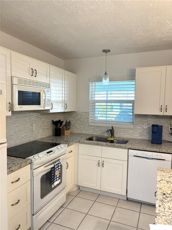A kitchen features white cabinets, granite countertops, a tile backsplash, and white appliances — 2115 9TH AVENUE W UNIT 6B, BRADENTON, FL