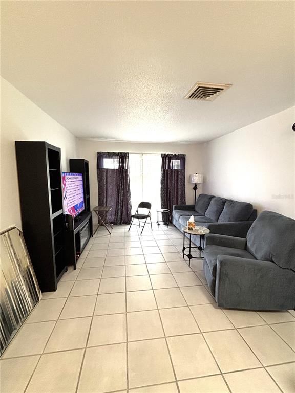 A living room features light tile flooring, a dark sofa and armchair, and a television console — 2115 9TH AVENUE W UNIT 6B, BRADENTON, FL