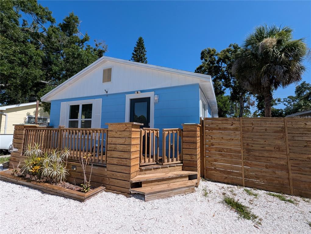A light blue house with a wooden deck and privacy fence sits on a gravel lot — 5005 NEWTON AVENUE S, GULFPORT, FL