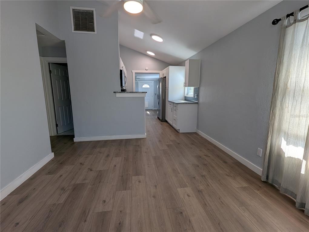 A kitchen and living area with light gray walls, wood-look flooring, and a vaulted ceiling — 5005 NEWTON AVENUE S, GULFPORT, FL