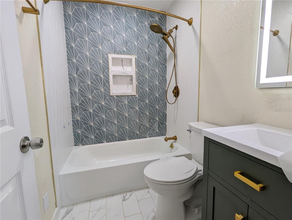 A bathroom features a blue geometric tiled shower wall, gold fixtures, and a dark vanity — 5005 NEWTON AVENUE S, GULFPORT, FL