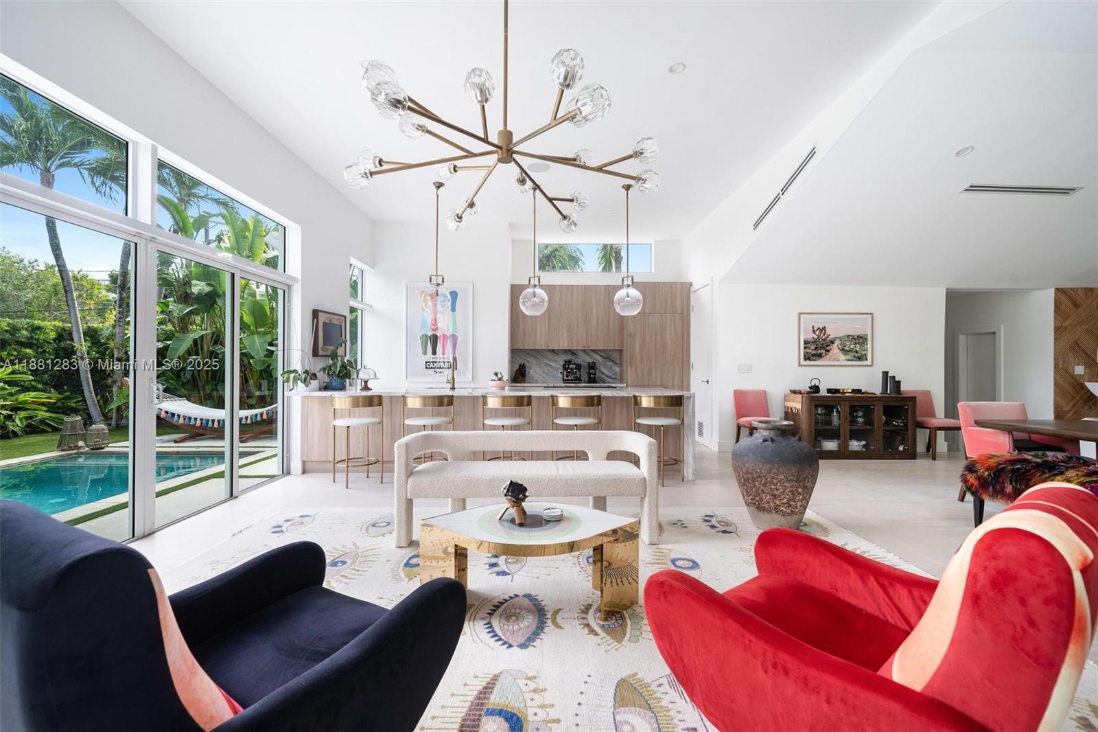 A modern living room and kitchen area features a large chandelier, pool view, and colorful furniture — 520 E Dilido Dr, Miami Beach FL 33139, MIAMI BEACH, FL