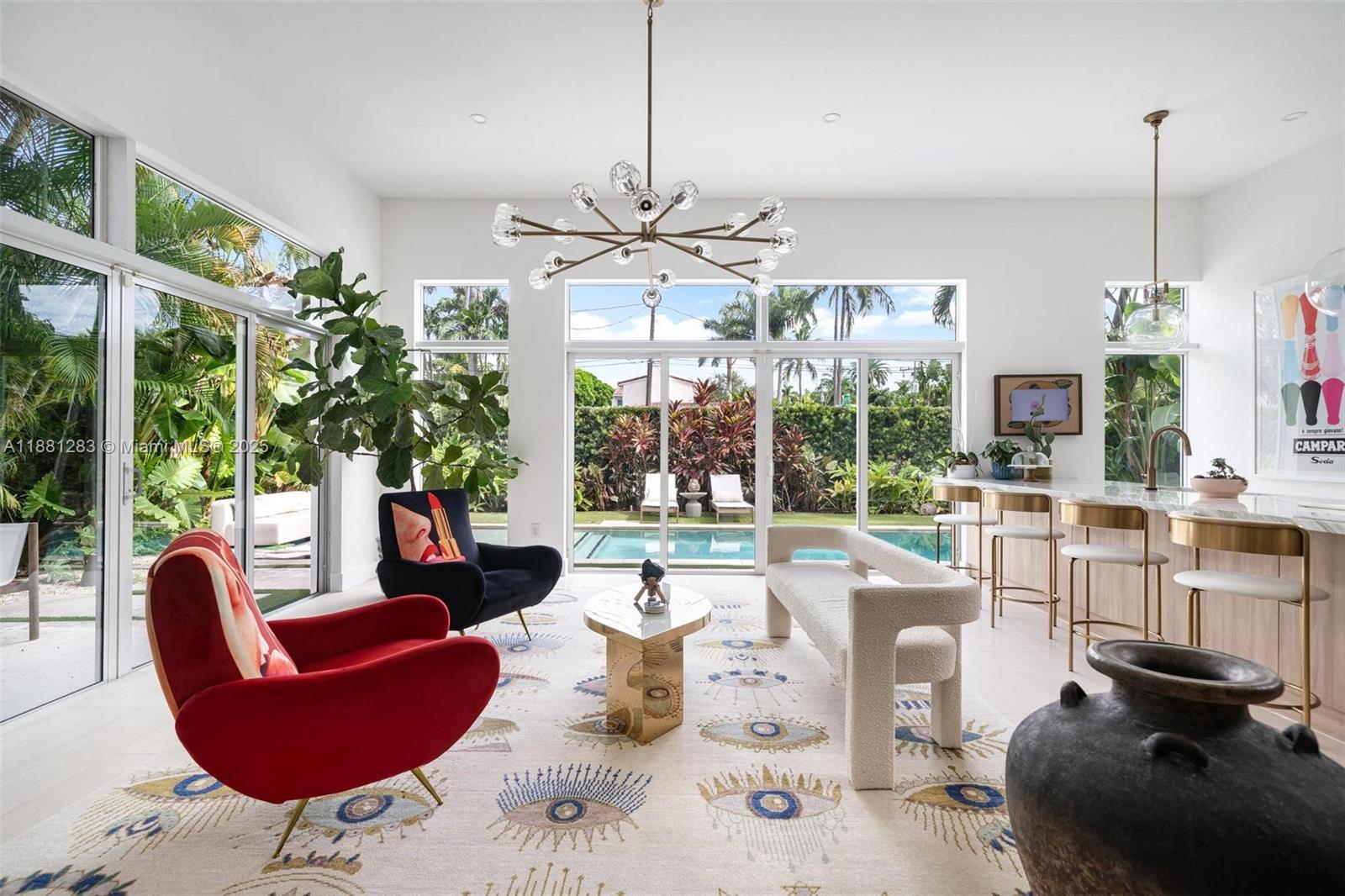 A bright living room features a modern chandelier, patterned rug, and floor-to-ceiling windows overlooking a pool — 520 E Dilido Dr, Miami Beach FL 33139, MIAMI BEACH, FL