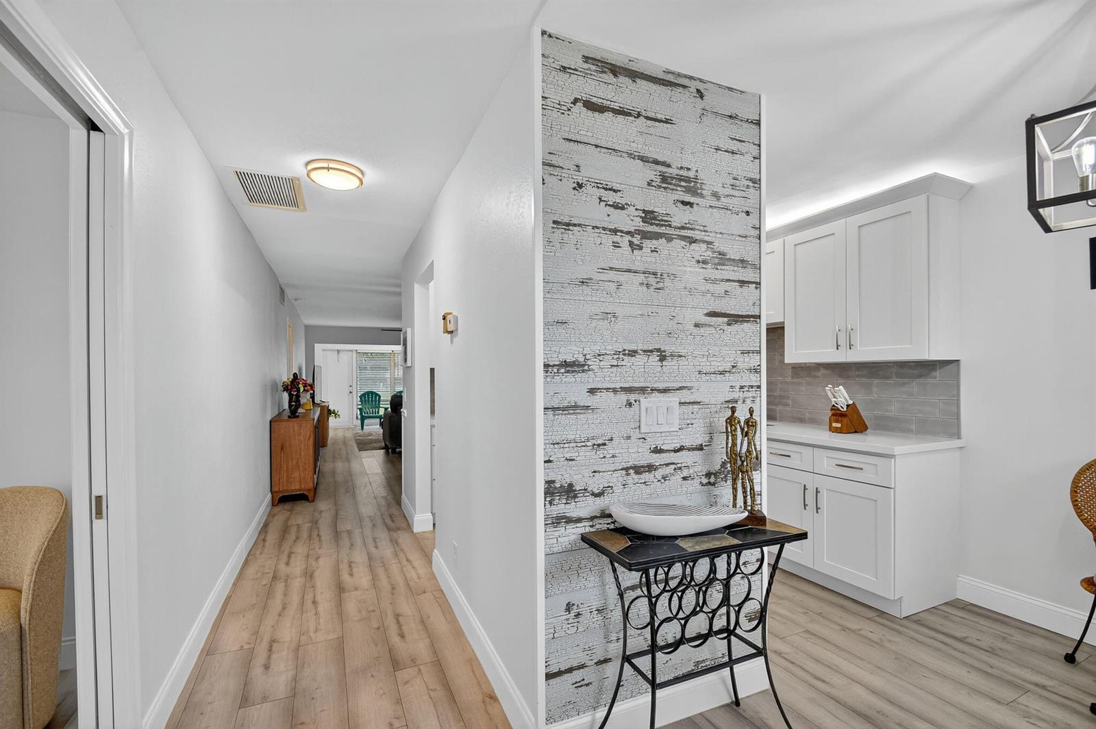 A hallway leads to a living area past a wall with distressed wood-look wallpaper — 2411 Papaya Drive # 103, Delray Beach FL 33445, DELRAY BEACH, FL