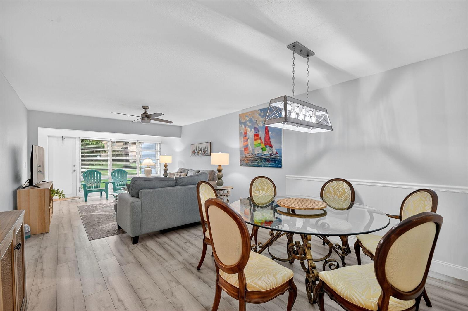 A living and dining area features light wood flooring, a glass-topped table, and gray furniture — 2411 Papaya Drive # 103, Delray Beach FL 33445, DELRAY BEACH, FL
