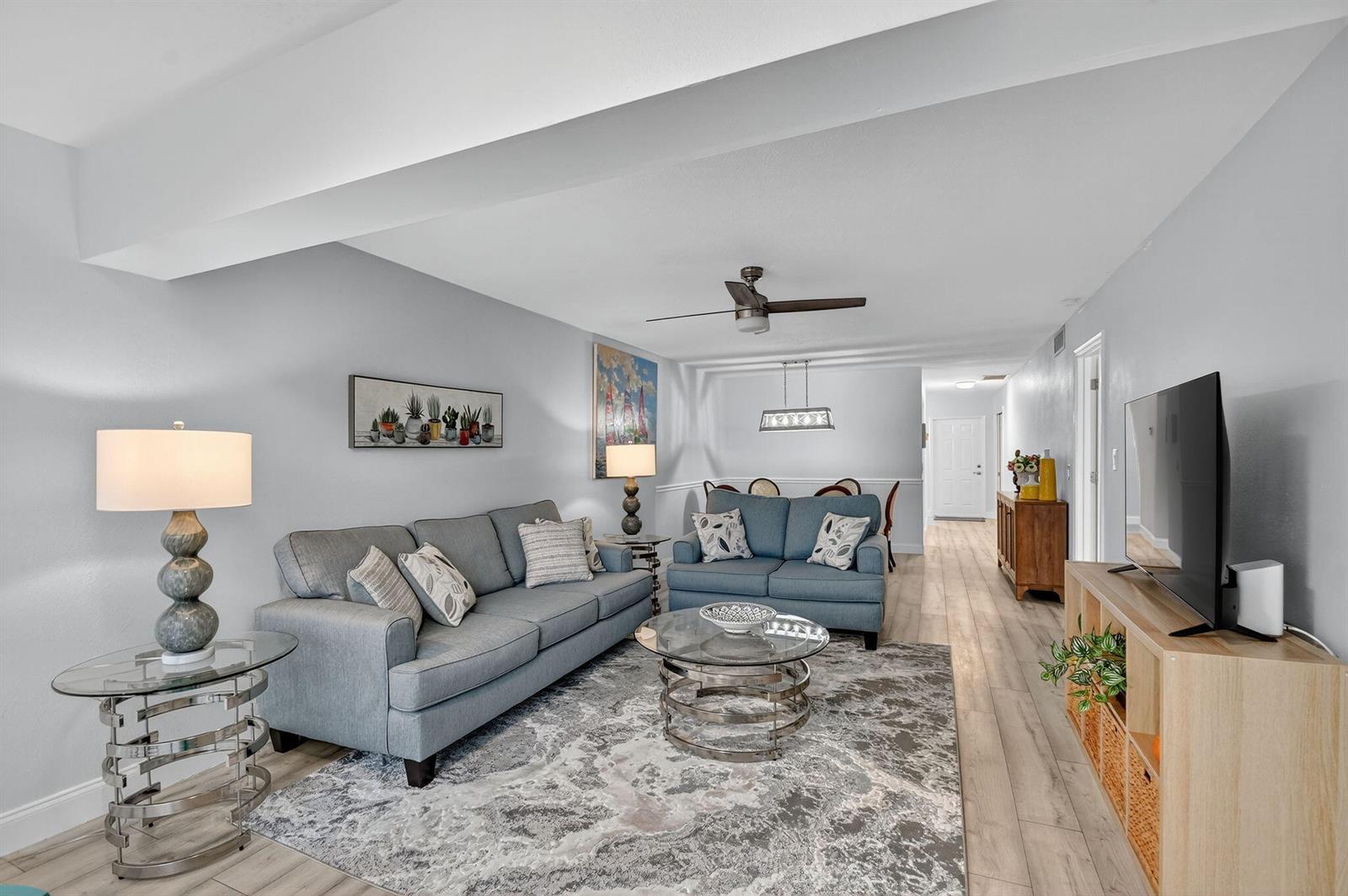 A living room features a grey sofa, a loveseat, a glass coffee table, and wood-look flooring — 2411 Papaya Drive # 103, Delray Beach FL 33445, DELRAY BEACH, FL