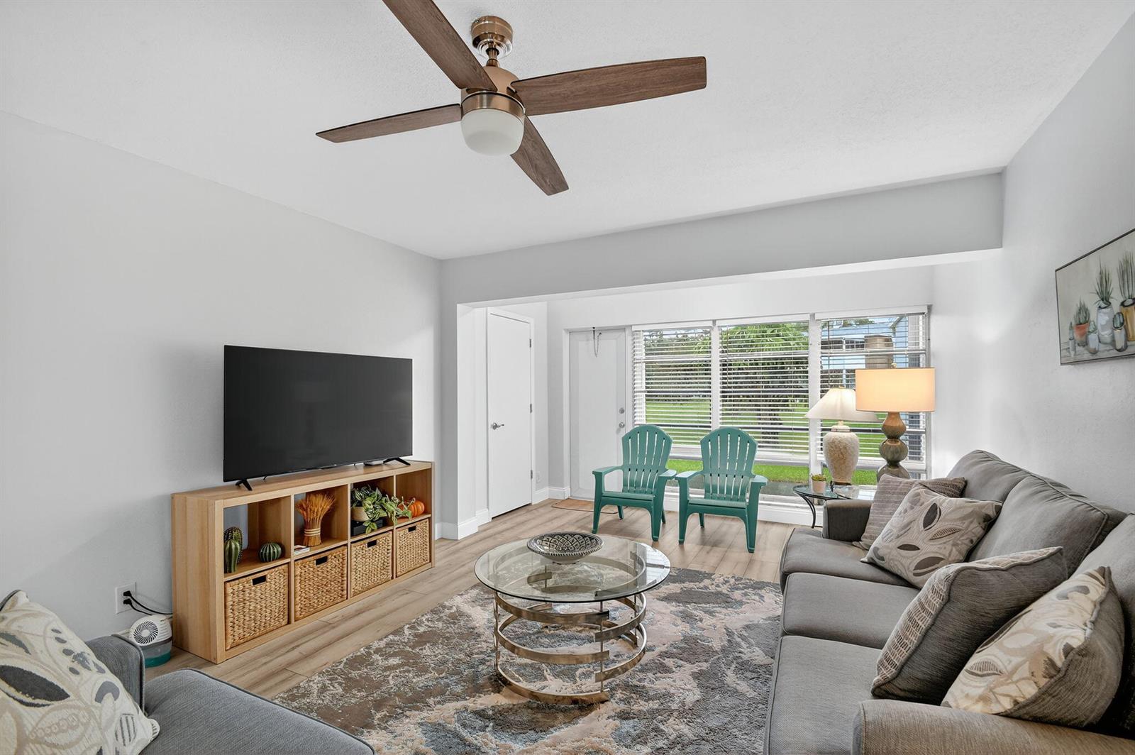 A living room features a grey sofa, a glass coffee table, and two teal chairs — 2411 Papaya Drive # 103, Delray Beach FL 33445, DELRAY BEACH, FL