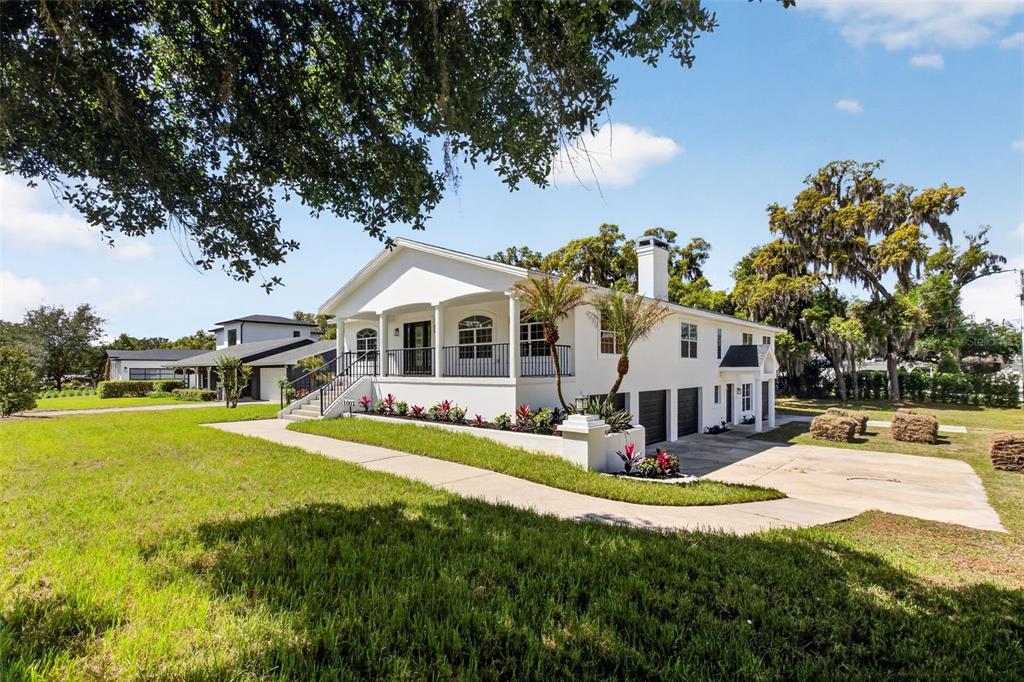 A white elevated house with a front porch and a concrete driveway under large trees — 1002 OAKDALE STREET, WINDERMERE, FL