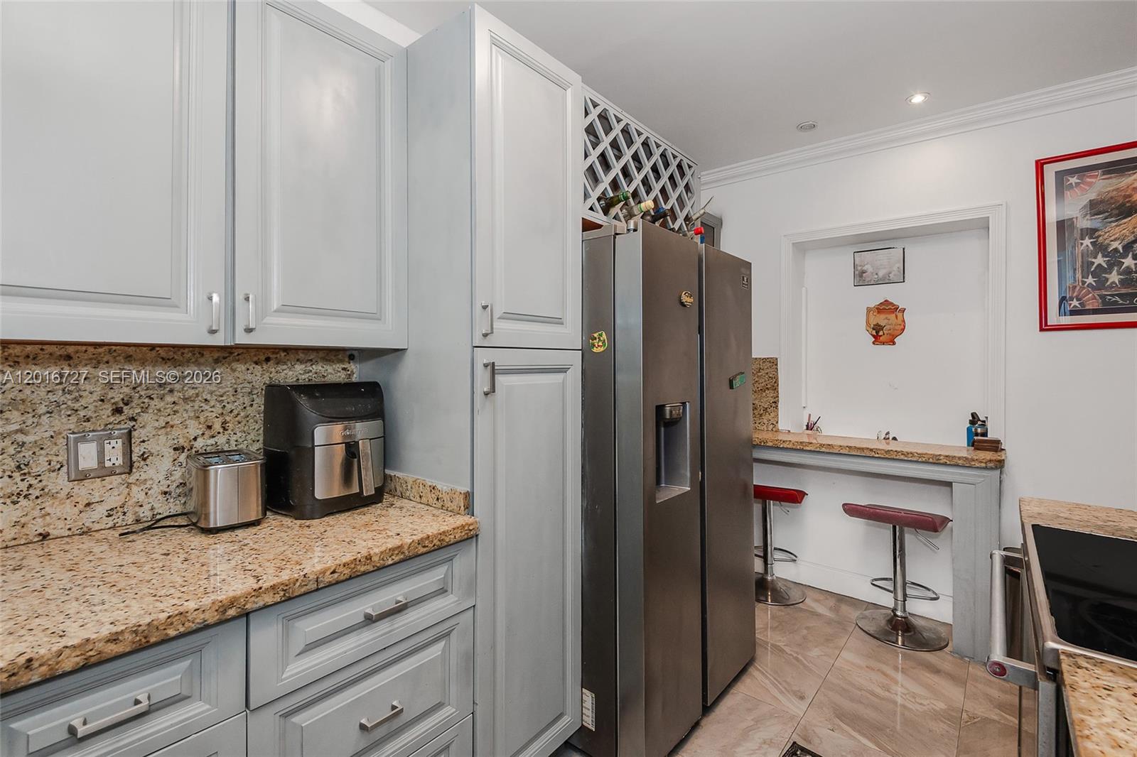 A kitchen features light gray cabinets, granite countertops, a stainless refrigerator, and a breakfast bar — 13485 NE 9th Ave, North Miami FL 33161, NORTH MIAMI, FL