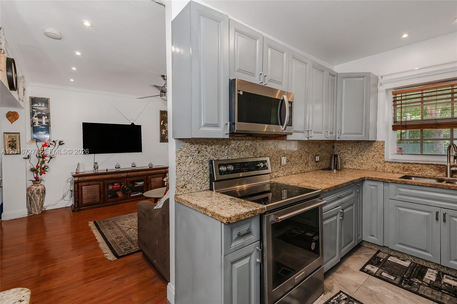 A kitchen with grey cabinets and granite countertops opens into a living room with hardwood floors — 13485 NE 9th Ave, North Miami FL 33161, NORTH MIAMI, FL