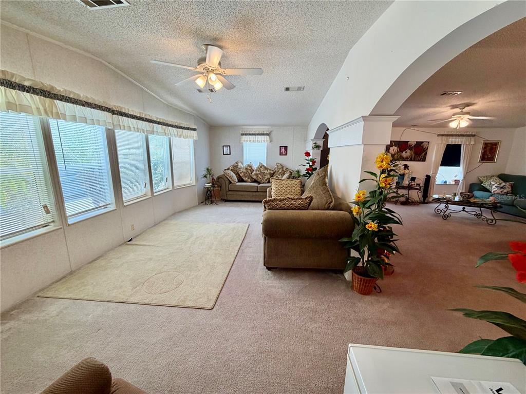 A spacious living area with beige carpeting, a ceiling fan, and large windows — 34066 AVOCADO DRIVE N, PINELLAS PARK, FL